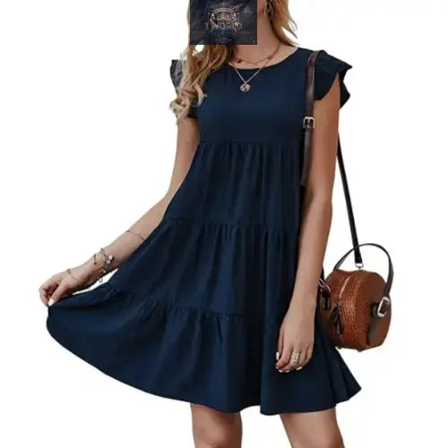 Short navy blue flowy tiered dress with ruffled cap sleeves - Elegant loose-fit summer mini dress for women with a round neckline - Styled with a brown leather bag - ALL IN 1 WORLD