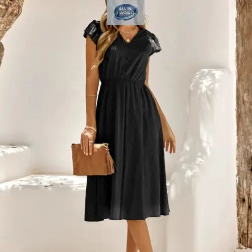 Full front view of an elegant black Swiss dot midi dress featuring a V-neckline and ruffled cap sleeves - Timeless flowy summer dress for women with an elasticated waist - Styled with a brown leather clutch - ALL IN 1 WORLD